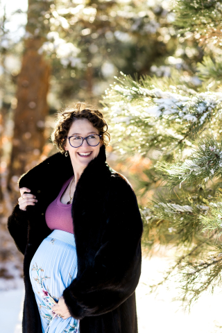 A portrait of a pregnant woman in a fur coat standing in snowy woods of Denver, CO, captures the anticipation and joy as she waits to welcome her new baby.