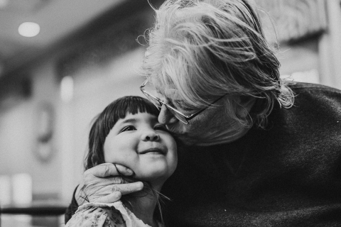 A lifestyle photographer took a black and white picture in Kansas City of a sweet child receiving kisses from Grandma, who is joyful and has a warm smile.
