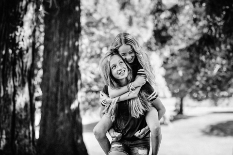 The picture taken by a photographer in a Northern California park shows two sisters playing, with one giving the other a piggyback ride, surrounded by big, old trees.