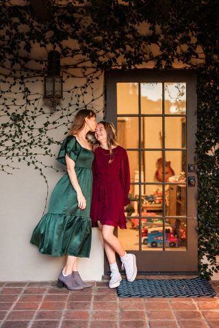 In Santa Barbara, California, a mother and her daughter share a sweet kiss on their porch during the Christmas holiday, standing by a door that gives a glimpse of their cozy home inside.