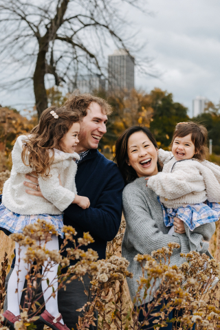 In Chicago, IL, a family with two kids smiles while enjoying a cloudy fall day outside surrounded by nature, captured by a lifestyle photographer.